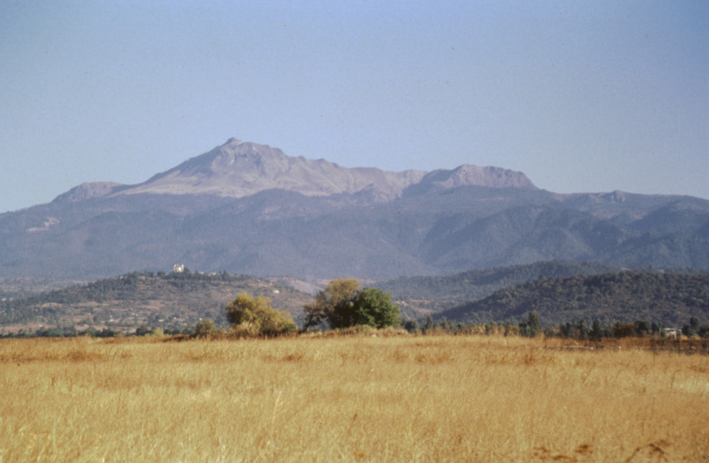 The southern flanks of Nevado de Toluca are seen here from near the town of Coatepec, with the summit peak of El Fraile to the left. The photo clearly shows the tree line on Toluca at about 4,000 m. Massive block-and-ash flows about 37,000 and 28,000 years ago extended down the southern flanks and beyond Coatepec. The hills in the foreground represent semi-vertical faces of faults forming a complex set of horst and graben structures. Photo by José Macías, 1997 (Universidad Nacional Autónoma de México).