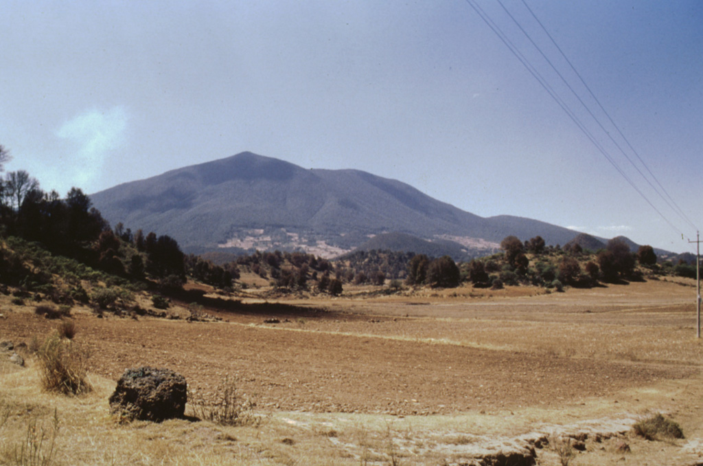 The tree-covered hills in the foreground of this view of Jocotitlán from the NE are the steep lobate front of a massive debris avalanche deposit produced by partial collapse of the volcano. This catastrophic collapse was radiocarbon dated to about 9,690 years ago. The avalanche traveled a maximum distance of 12 km and covered an area of 80 km2. The 2.8 km3 avalanche deposit is overlain by pyroclastic surge and airfall pumice deposits that were erupted immediately following the collapse. Photo by José Macías, 1997 (Universidad Nacional Autónoma de México).