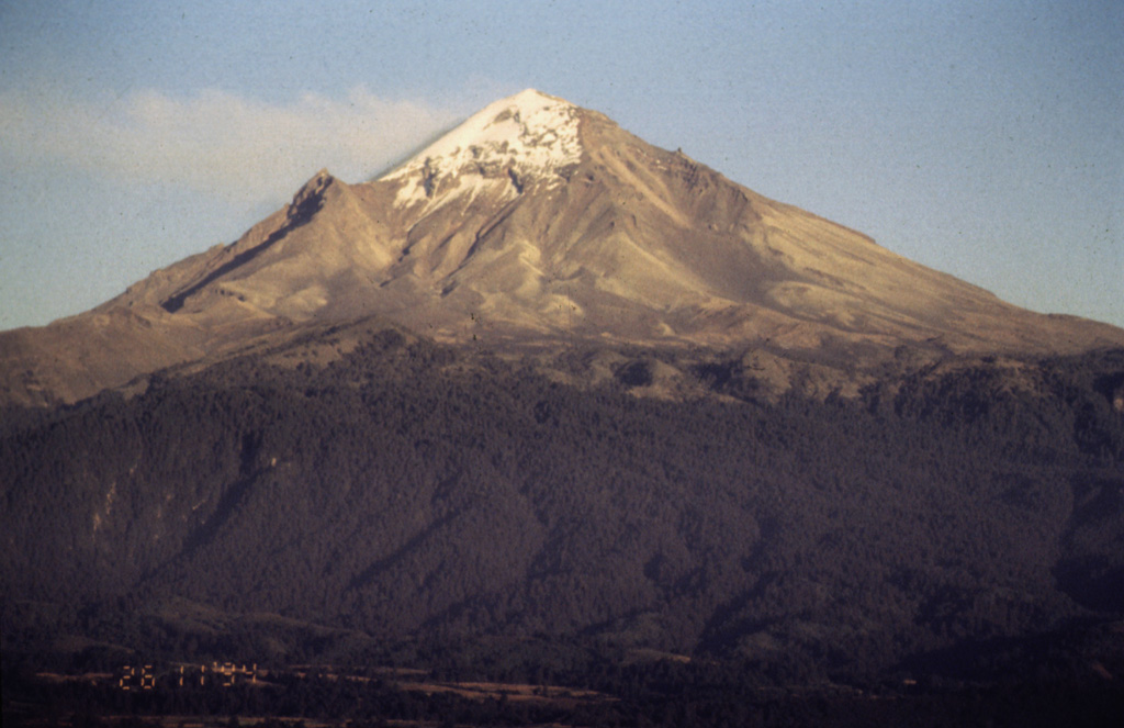 The western flank of Popocatépetl is seen here in November 1994, a little more than a month prior to its eruption on 21 December 1994. A faint gas plume is dispersing to the NE by predominant winds. The peak halfway down the left flank is Ventorrillo, a remnant of an older volcanic center preceding the construction of the modern edifice. Photo by José Macías, 1994 (Universidad Nacional Autónoma de México).