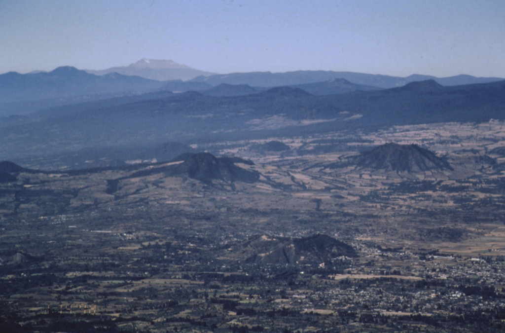 Cones of the Chichinautzin volcanic field in the foreground and middle distance are seen here looking to the west from Popocatépetl volcano. The large flat-topped volcano on the far horizon is Nevado de Toluca. The broad Chichinautzin volcanic field covers a 90-km-wide area south of the Valley of Mexico between the base of the Sierra Nevada (containing Popocatépetl and Iztaccíhuatl) and the eastern flank of Nevado de Toluca. Photo by José Macías, 1998 (Universidad Nacional Autónoma de México).