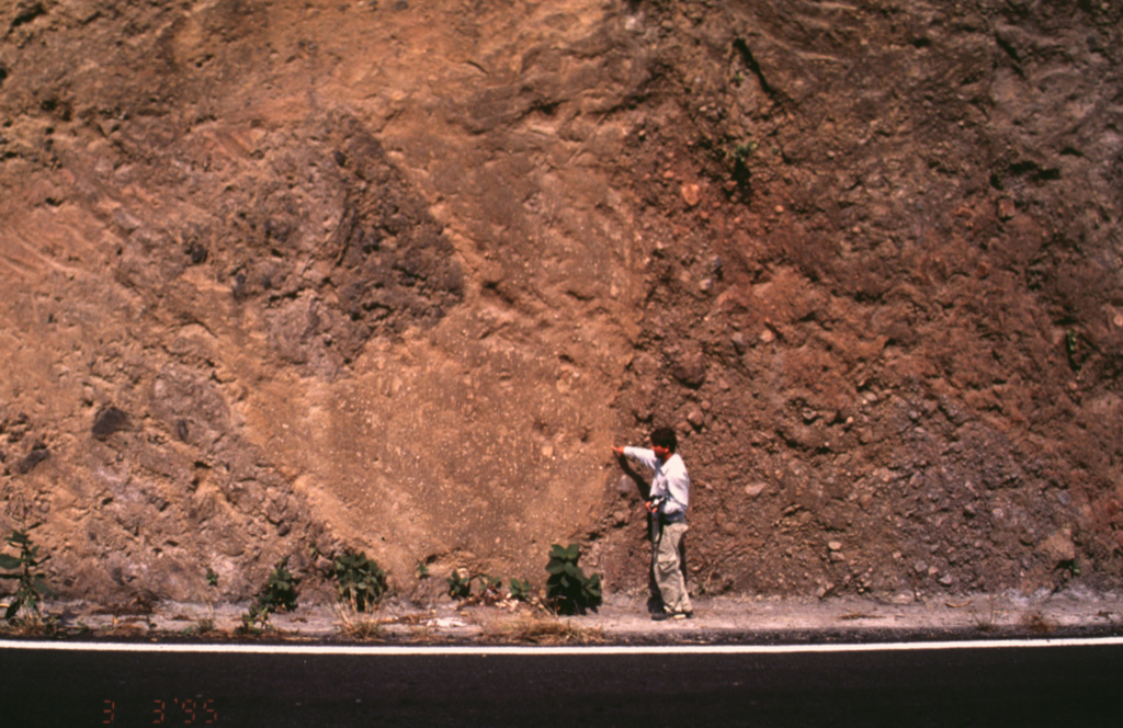 Popocatépetl volcano has been partially destroyed on at least three occasions by massive flank collapse events that have produced voluminous debris avalanche deposits that extend long distances primarily to the south. This roadcut exposes an outcrop of the youngest debris avalanche deposit, which was emplaced about 23,000 years ago. The person for scale points to the edge of a large block of material from the volcano that was carried within finer-grained material. Photo by José Macías, 1995 (Universidad Nacional Autónoma de México).