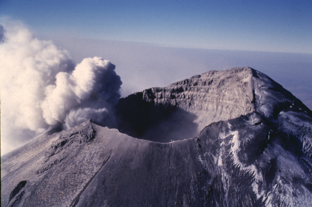 An ash plume erupts from the small vents along the eastern edge of the crater in this 11 March 1996 photo. The plume rises up to the crater rim then is dispersed by the predominant winds to the east, becoming detached from the summit crater after the explosion ends. The glacier on the NW (right) side of the crater is partly covered with dark gray ash from previous eruptions. Photo by José Macías, 1996 (Universidad Nacional Autónoma de México).