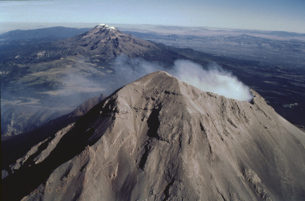 Iztaccíhuatl and Popocatépetl are part of the N-S-trending Sierra Nevada range SE of Mexico City. Iztaccíhuatl, in the center of the range, is to the upper left, and Popocatépetl is in the foreground at the southern extremity of the range. The Sierra Nevada separates the Valley of Mexico from the Puebla basin, which can be seen to the east. Ashfall from recent eruptions covers the summit snow cover this 1996 photo. Photo by José Macías, 1996 (Universidad Nacional Autónoma de México).