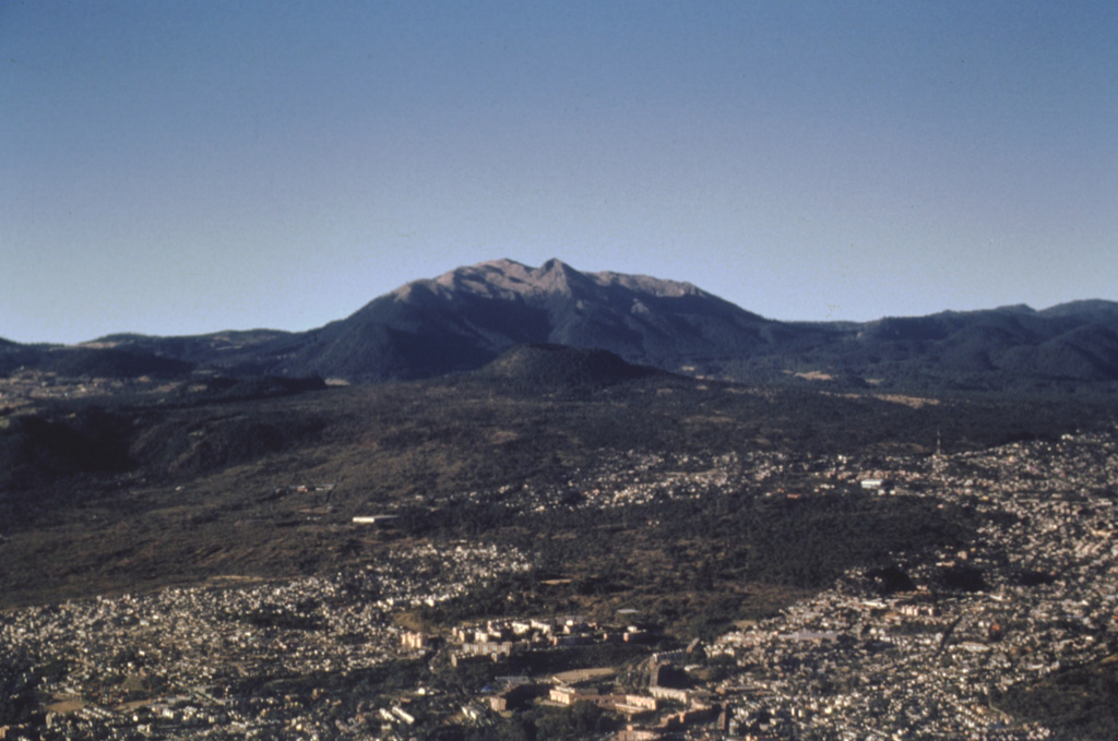The small Xitle scoria cone in the center of the photo is directly below Volcán Ajusco, the large lava-dome complex on the horizon, and was the source of a voluminous lava flow about 1,670 years ago. The 3.2 km3 flow traveled 13 km north and underlies much of the forested area in the middle of the photo as well as the southern part of Mexico City in the foreground. The flow covered the Preclassic city of Cuicuilco, one of the oldest archaeological sites in central México, and underlies the campus of the National University of México (UNAM). Photo by José Macías, 1996 (Universidad Nacional Autónoma de México).