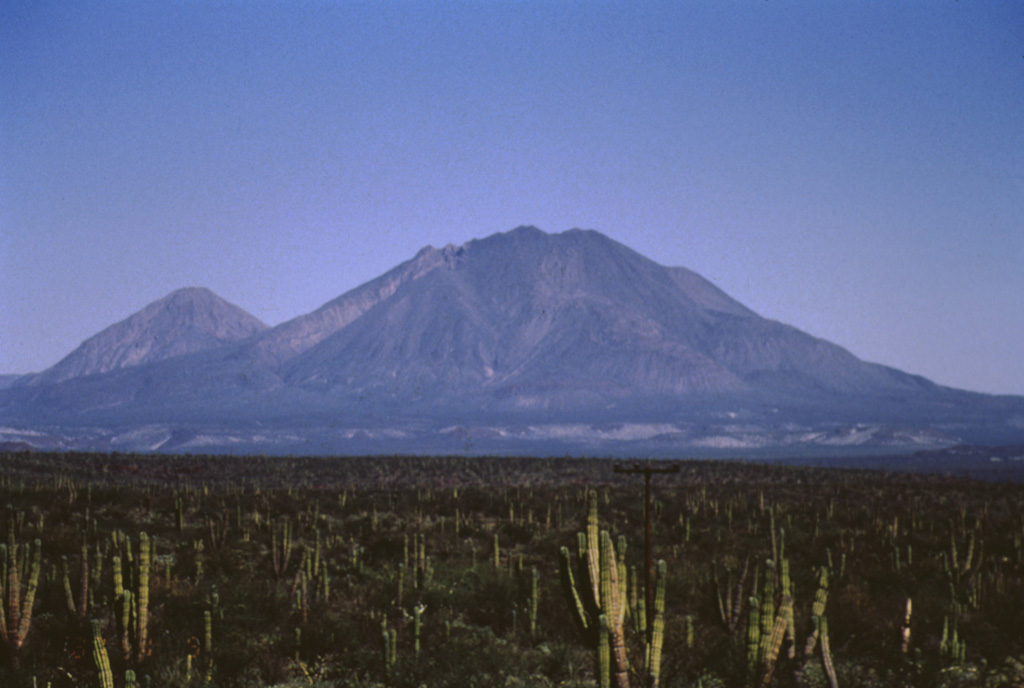 The two most prominent peaks of the Tres Vírgenes volcanic complex in central Baja California are seen here from the SSW. The peak to the left is El Azufre, a dacite lava dome complex. La Vírgen (right), consisting of andesite lava domes and flank scoria cones, formed more recently and has a more complicated history. It has erupted from both summit and flank vents and has produced both Plinian explosive eruptions and dacitic and andesitic lava flows. Photo by José Macías, 1995 (Universidad Nacional Autónoma de México).