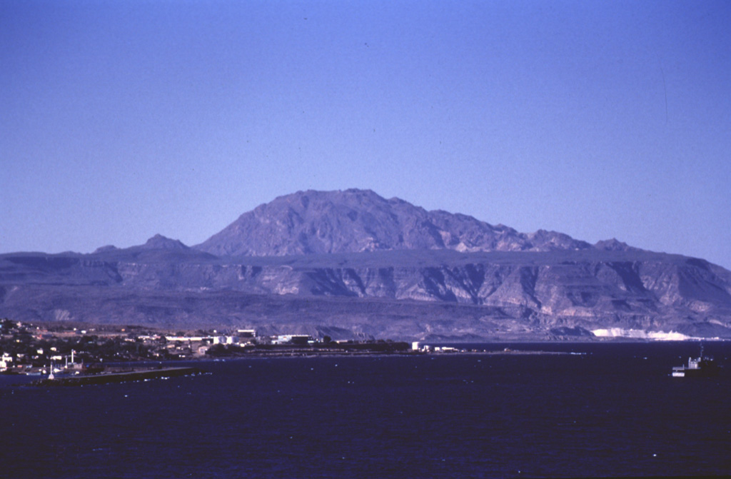 The early Pleistocene La Reforma caldera lies NW of the town of Santa Rosita (left) on the Gulf of California.  The roughly 10-km-wide caldera contains a central dome (center horizon) made of resurgent basement rocks.  Ignimbrite outflow sheets form flat surfaces and scarps.  The age of the caldera was determined by the K-Ar method to be between 1.6 and 1.4 Ma.  The eruption of andesitic and dacitic ring-fracture lava domes followed.  Andesitic lava flows were erupted on the flanks of the caldera both before and after caldera formation. Photo by José Macías, 1995 (Universidad Nacional Autónoma de México).