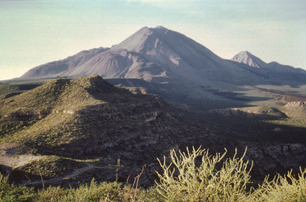 This view from the SE shows the Tres Vírgenes volcanic group, which is aligned in a SW-NE direction. Volcanism has migrated to the SW from the oldest peak El Viejo (far right) through El Volcán Azufre to La Vírgen (center), the highest peak. The ridges on the left flank of La Vírgen are rhyodacite lava flows from a major eruption; the smooth hills in the foreground are Quaternary ignimbrite sheets probably related to the Pleistocene La Reforma caldera to the east.  Photo by José Macías, 1995 (Universidad Nacional Autónoma de México).
