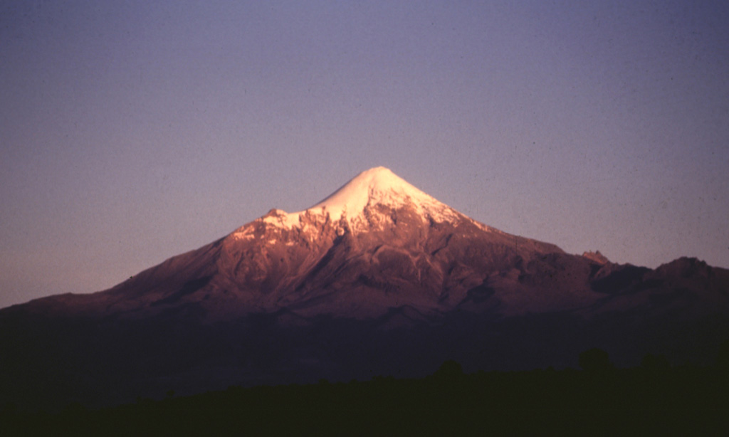The evening sun illuminates the Pico de Orizaba western flank. The smaller peak to the left is the NW-flank peak of Sarcofago. The NW-dipping lavas of Sarcofago, which is part of the Espolón de Oro edifice, were exposed by edifice collapse. The collapse event forming a horseshoe-shaped crater, inside which the modern cone was constructed. Photo by José Macías, 1995 (Universidad Nacional Autónoma de México).