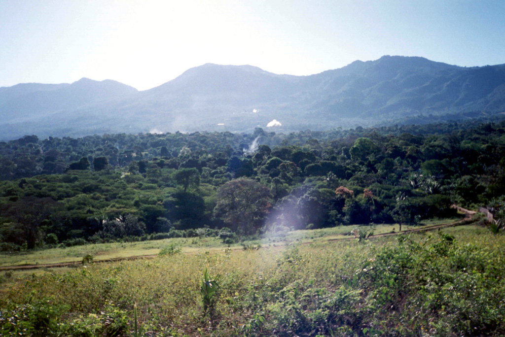 The Laguna Las Ninfas-Laguna Verde volcanic complex is seen here from the NW with steam plumes of the Ahuachapán geothermal field in the midground. The 5-km-wide Concepción de Ataco caldera formed during the late Pleistocene following the eruption of about 70 km3 of pyroclastic flows and airfall tephra. Flat-topped Laguna Verde at the center of the photo and Las Ninfas at the right are post-caldera cones. Cerro Cuyanausul (left) was constructed prior to caldera formation and lies to the east of the caldera. Photo by Pat Dobson, 1999 (Lawrence Berkeley National Laboratory).