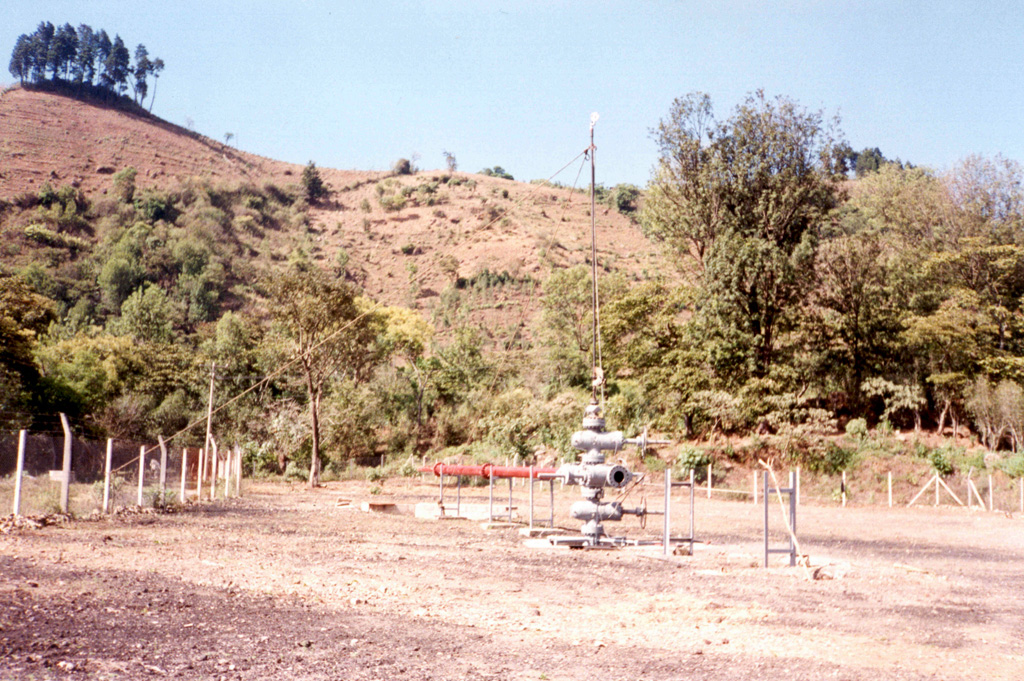 The geothermal well AMF-1 within Amatitlán caldera near Pacaya is seen here with the Laguna Caldera fault scarp in the background. Geothermal development within this 14 x 16 km Pleistocene caldera was providing electrical power to Guatemala's capital city, which overlies deposits from Amatitlán caldera. Photo by Pat Dobson, 1997 (Lawrence Berkeley National Laboratory).