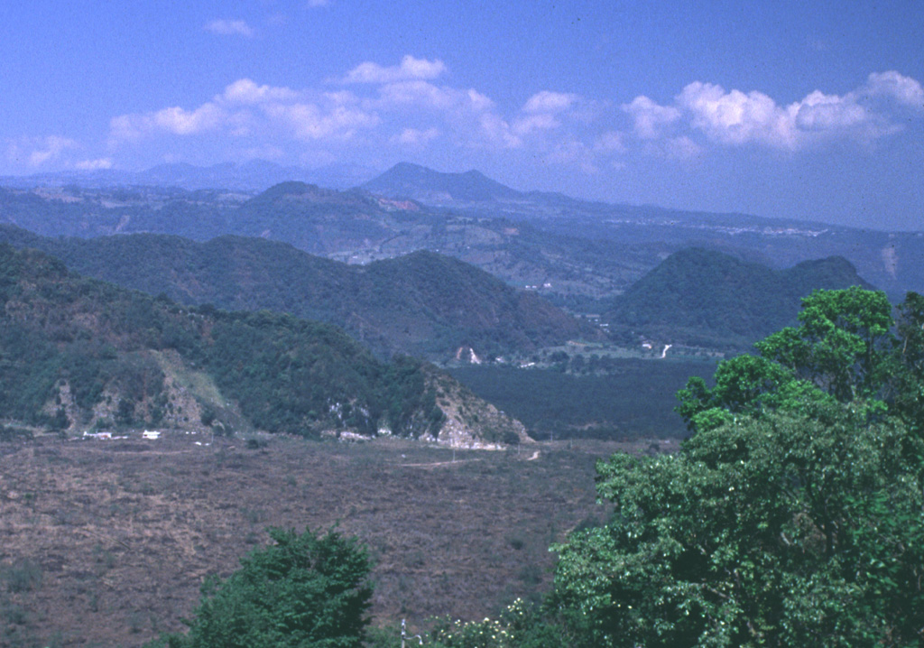 The Naolinco Volcanic Field consists of a broad area of scattered Quaternary cones and associated lava flows north of the city of Jalapa, the capital city of the state of Veracruz. Cerro Acatlán in the distance is the largest cone, and is located NE of the town of Naolinco de Victoria. This and other nearby cones have fed lava flows that traveled to the S and SE. The barren area in the foreground is part of the Río Naolinco lava flow, which erupted from vents on the NE flank of Cofre de Perote volcano. Photo by Lee Siebert, 1999 (Smithsonian Institution).