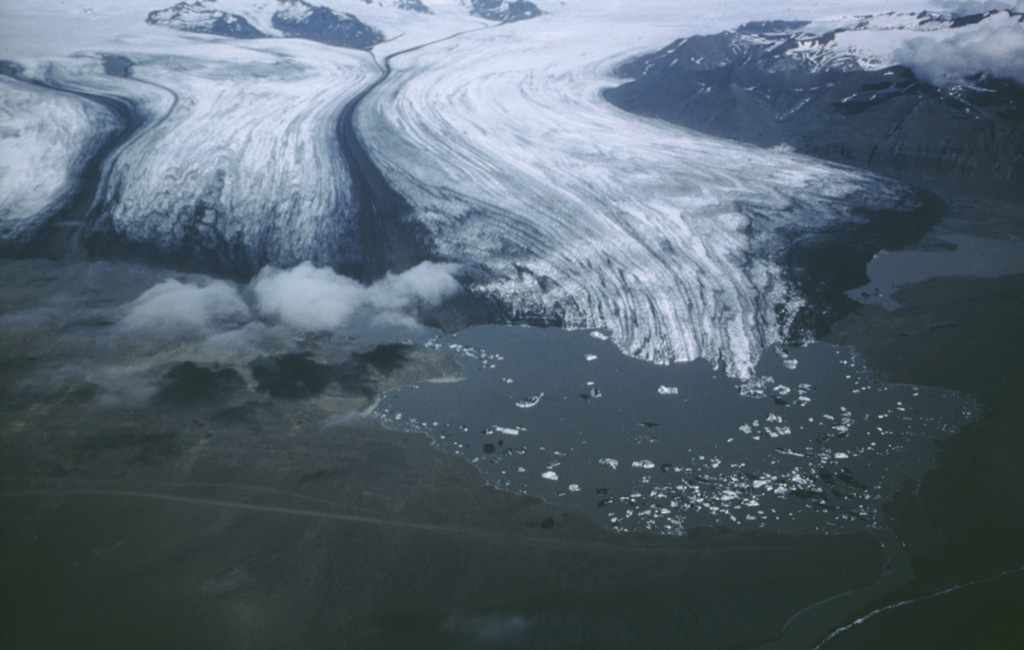 The subglacial Esjufjöll volcano rises (upper left) above the Breidamerkurjökull glacier, with its prominent medial moraines. Icebergs calved from the glacier can be seen floating in Jökulsárlón lake, which drains into the Atlantic Ocean (extreme lower right). Esjufjöll is located at the SE part of the Vatnajökull icecap, north of Öræfajökull volcano. Photo by Oddur Sigurdsson, 1986 (Icelandic National Energy Authority).