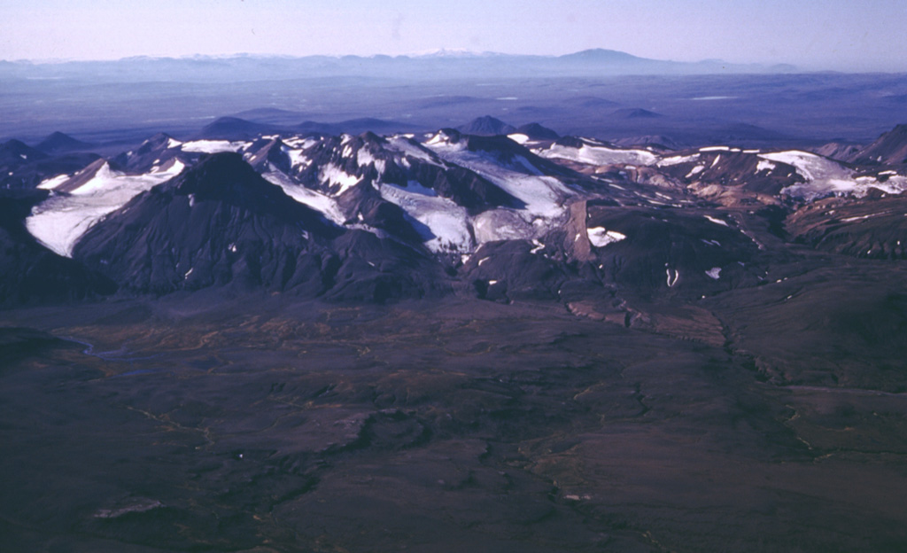 The flanks of the largely Pleistocene rhyolitic central volcano Kerlingarfjöll have been deeply dissected by glaciers, giving it a rugged appearance. This approximately 10-km-wide volcanic edifice is seen here from the NNE, separated by a topographic low (foreground) from Hofsjökull. A Holocene eruption between the two edifices produced the Illahraun lava flow. This lava flow travelled more than 20 km S and is petrologically linked to Hofsjökull. Kerlingarfjöll has a large geothermal area with vigorous fumaroles. Photo by Oddur Sigurdsson, 1998 (Icelandic National Energy Authority).