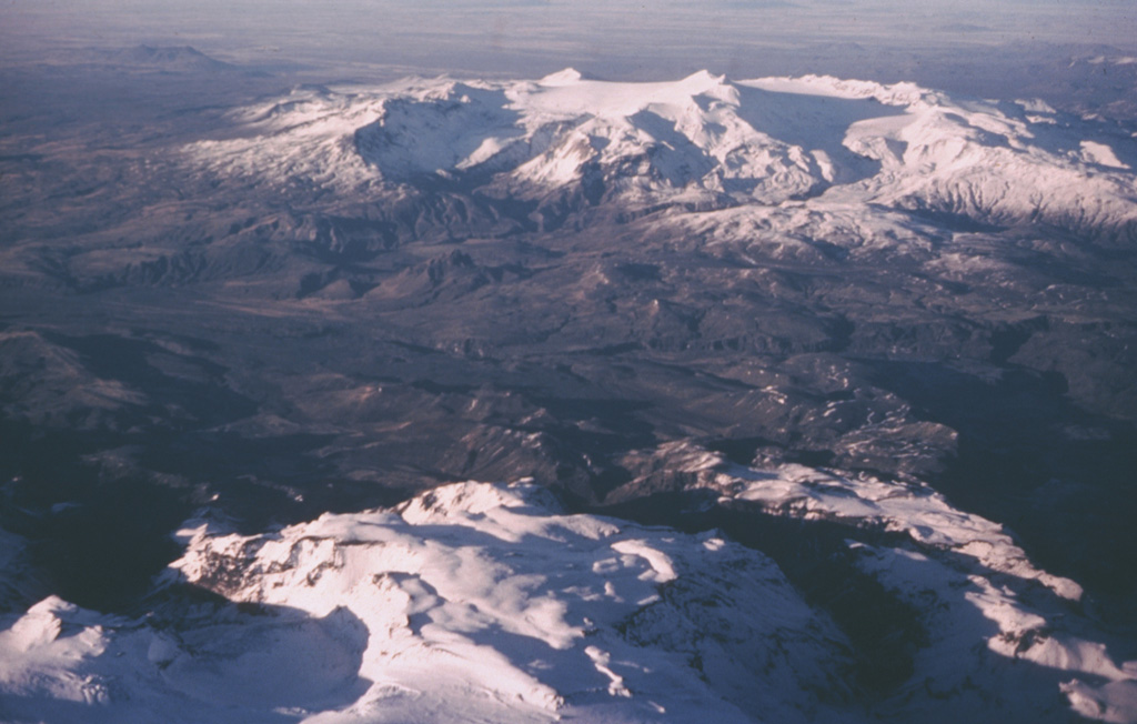 The broad massif of Tindfjallajökull is seen here from the ESE looking into the open 5 x 7 km summit caldera, with a rugged two-peaked rhyolitic dome in the center.  The NW rim of the caldera is overtopped by the Tindfjallajökull icecap, which forms the smooth flat surface at the summit. Several small effusive eruptions occurred at the beginning of the Holocene. Photo by Oddur Sigurdsson, 1976 (Icelandic National Energy Authority).