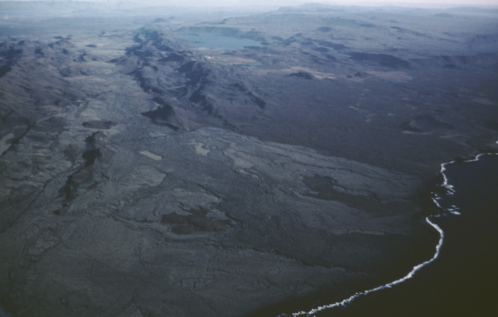 The Krýsuvík-Trölladyngja volcanic system consists of NE-SW-trending crater rows and small shield volcanoes cutting the central Reykjanes Peninsula west of Kleifarvatn lake (top center). Several eruptions have taken place since the settlement of Iceland, including the emplacement of a large lava flow from the Ogmundargigar crater row around the 12th century. The lava flow was confined to the valley between the two parallel ridges (top left), before reaching the southern coast of the Reykjanes Peninsula (lower right) along a broad front. Photo by Oddur Sigurdsson, 1983 (Icelandic National Energy Authority).