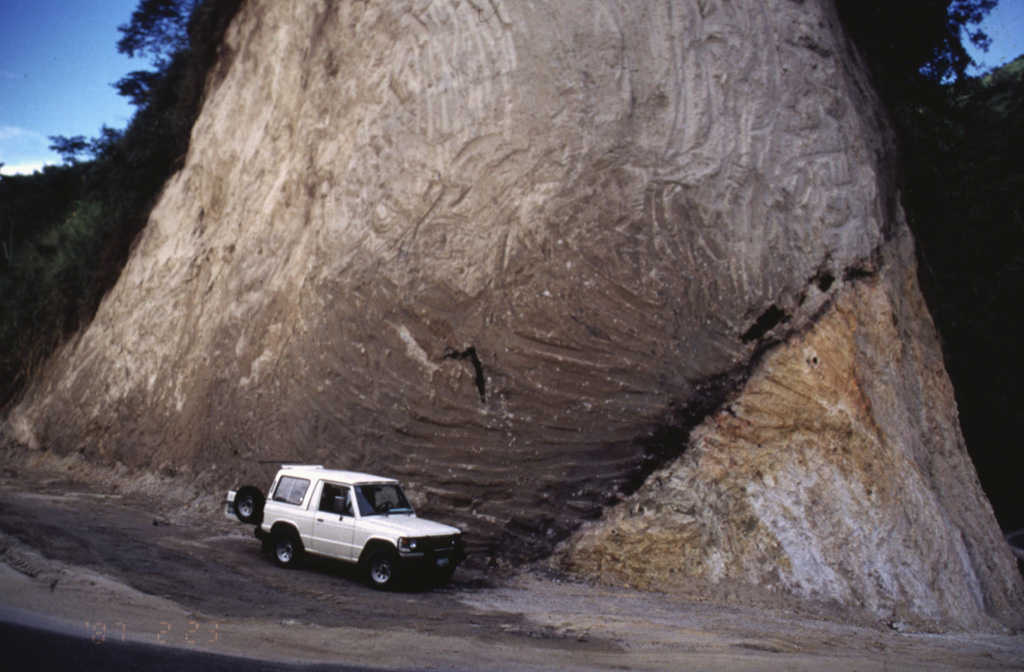 A road cut exposes a pyroclastic flow deposit (left) overlying older granite (lower right). The dark zone dipping away from the front of the jeep, at the base of the pyroclastic flow deposit, are trees charred by the hot pyroclastic flow. This site is located along the road that connects the cities of Ibague and Cajamarco, close to the town of El Boqueron, about 12 km from Cerro Machín volcano. Photo by José Macías, 1996 (Universidad Autómona de México).