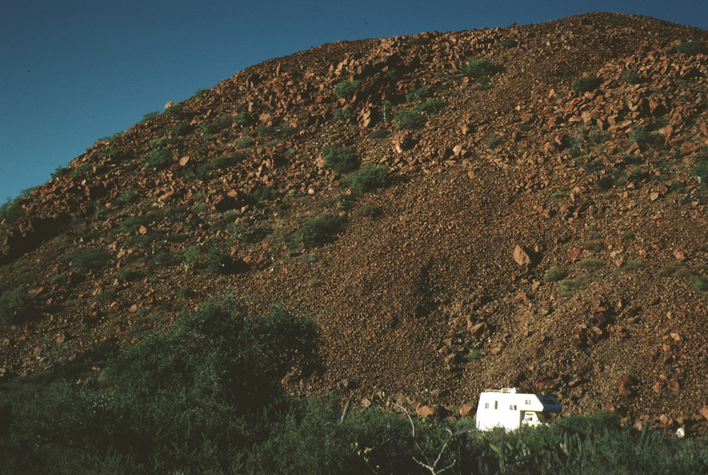 The steep margin of a thick basaltic andesite lava flow is seen from near State Highway 1 in central Baja California with a vehicle for scale. The sparsely vegetated flow is of probable Holocene age and is one of many recent lava flows of the San Borja Volcanic Field. Photo by Andy Saunders, 1984 (University of Leichester).