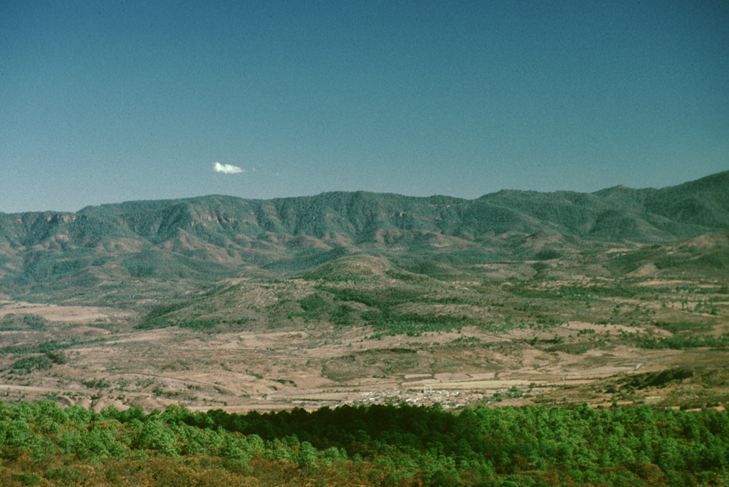 This photo looks east from Las Tortugas volcanic center towards the town of Atenguillo.  Low hills just behind and sightly to the left of Atenguillo are eroded trachybasaltic lava flows of Pliocene age.  The ridge in the background exposes late Cretaceous ashflow tuffs that make up the Atenguillo graben walls. Photo by Paul Wallace, 1998 (University of California Berkeley).