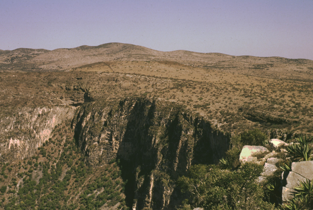 The largest and best-known maar of the Ventura volcanic field is Joya Honda.  The eastern wall of the 850 x 1100 m wide, 300-m-deep maar is seen here from the south rim.  The maar was erupted through Cretaceous limestones, the cliff-forming units in the crater wall, about 1.1 million years ago. The Ventura volcanic field consists of a group of maars and pyroclastic cones located immediately NE of the city of San Luis Potosí in the southern Basin and Range province of central México.   Photo by Jorge Aranda-Gómez, 1994 (Universidad Autónoma de México).