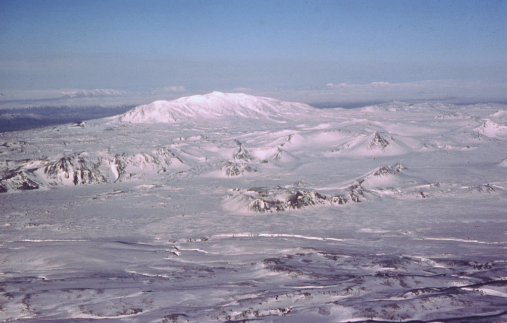 The Vatnafjöll volcanic system, seen as the rugged landscape cutting across the center of the image, is a 60-km-long, 9-km-wide chain of alkali basaltic fissures and crater rows located south of the more prominent Hekla volcano (center horizon). The elongate profile of Hekla is due to the presence of an elongate eruptive fissure parallel with the ridge, which has been the site of numerous Holocene eruptions. The Vatnafjöll fissure swarm is less frequently active than the Hekla edifice, but they are considered as part of the same volcanic system. About 50 Holocene lava flows are identified from the Vatnafjöll fissures, most recently about 1,200 years ago. Photo by Oddur Sigurdsson, 1977 (Icelandic National Energy Authority).