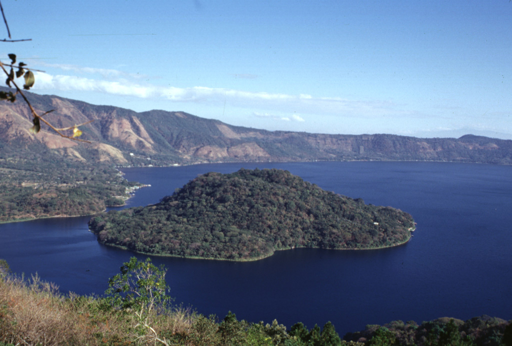 Cerro Grande is the largest of a series of post-caldera lava domes extruded along a NE-SW-trending line within Coatepeque caldera. The lava dome, seen here from the southern caldera rim, rises about 90 m above the lake surface and about 180 m above the lake floor. Photo by Paul Kimberly, 1999 (Smithsonian Institution).