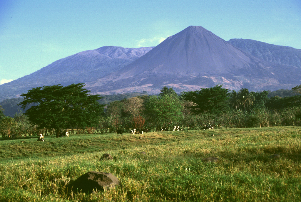 Izalco volcano was once known as the "Lighthouse of the Pacific" for its persistent incandescent nighttime eruptions. It was constructed on the southern flank of Santa Ana, whose broad summit is to the left. To the right is Cerro Verde, a scoria cone on the SE Santa Ana flank. Lava flows at the base if Izalco from both summit and flank vents and extend out to 7 km. Photo by Lee Siebert, 1999 (Smithsonian Institution).