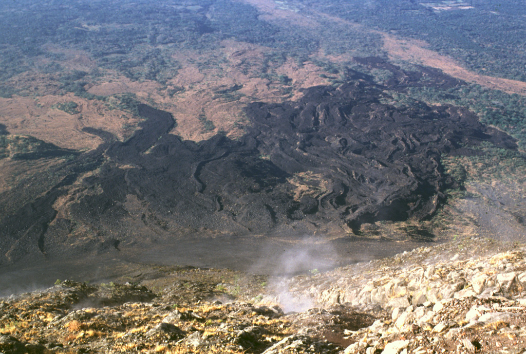 A lava flow field on the SW flank of Izalco is seen here from its summit. Levees define distinct flows of the lava field, which extends up to about 7 km from the summit. Most of the flows seen here were emplaced prior to 1954. Gas rises from fumaroles near the summit. Photo by Lee Siebert, 1999 (Smithsonian Institution).