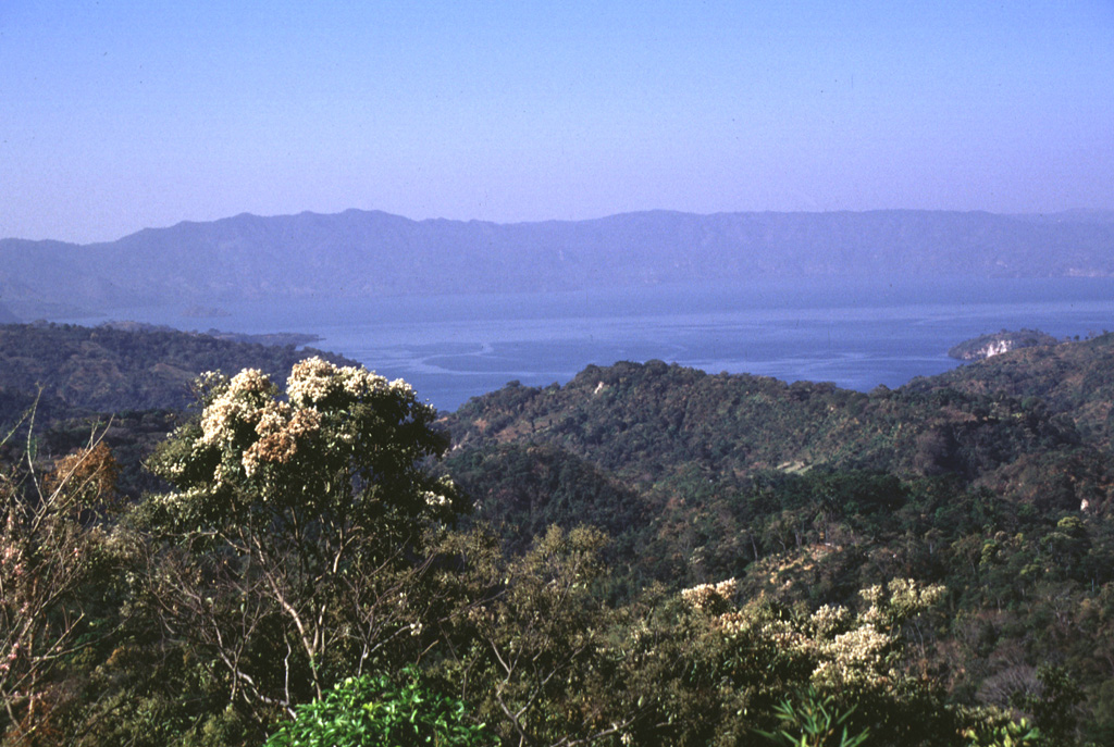 The 13 x 17 km Ilopango caldera is seen here from the NE with the southern caldera wall in the background. It formed during four major Quaternary eruptions, the last of which occurred about 1,500 years ago. The southern caldera wall rises about 500 m above the lake, which had a maximum depth of about 230 m when this photo was taken in 1999.  Photo by Lee Siebert, 1999 (Smithsonian Institution).