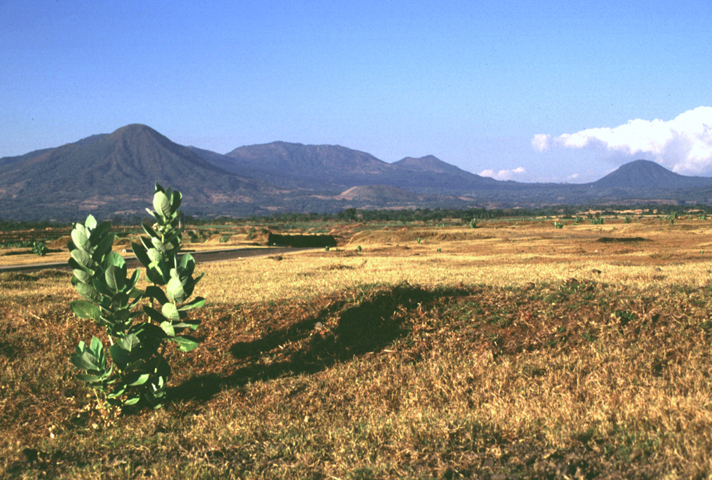 The rounded Volcan Taburete (far left) and the Tecapa volcanic massif rise to the NW above the Pacific coastal plain of El Salvador. The small Loma Pacha cone on the lower SE flank of Taburete (visible in the center of the image) produced a thick lava flow that traveled to SE. The rounded peak to the far right is Cerro Oromontique, a cone that erupted on the flank of El Tigre. Photo by Lee Siebert, 1999 (Smithsonian Institution).