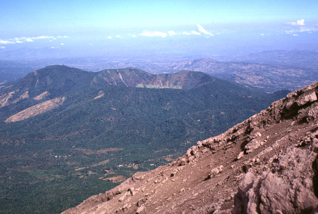 Chinameca volcano, also known as El Pacayal, is seen here to the NW from the barren upper flanks of San Miguel volcano.  Coffee plantations mantle the slopes of the 1300-m-high stratovolcano, which is truncated by a 2-km-wide caldera.  The high point of the caldera, Cerro el Pacayal, lies on the western rim (left-center) and rises about 450 m above the caldera floor.  The rounded peak of Cerro el Limbo at the left rises to above 1380 m, exceeding the height of the caldera rim.  Photo by Lee Siebert, 1999 (Smithsonian Institution).