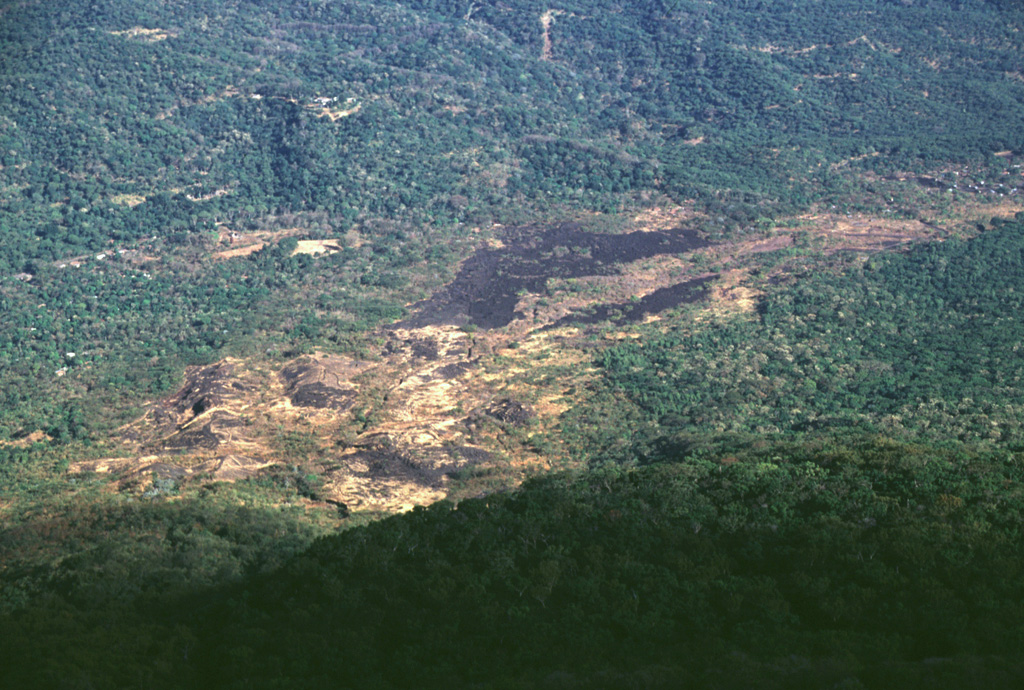 The sparsely vegetated basaltic lava flow cutting diagonally across the photo to the upper right was erupted from a NNW-flank vent in 1844.  The flow traveled initially to the NNW toward the broad saddle between San Miguel and Chinameca volcanoes and then was deflected to the NE.  It traveled in a narrow lobe as far as 8 km from the summit near the path of the present-day road between the town of San Jorge and the city of San Miguel. Photo by Lee Siebert, 1999 (Smithsonian Institution).