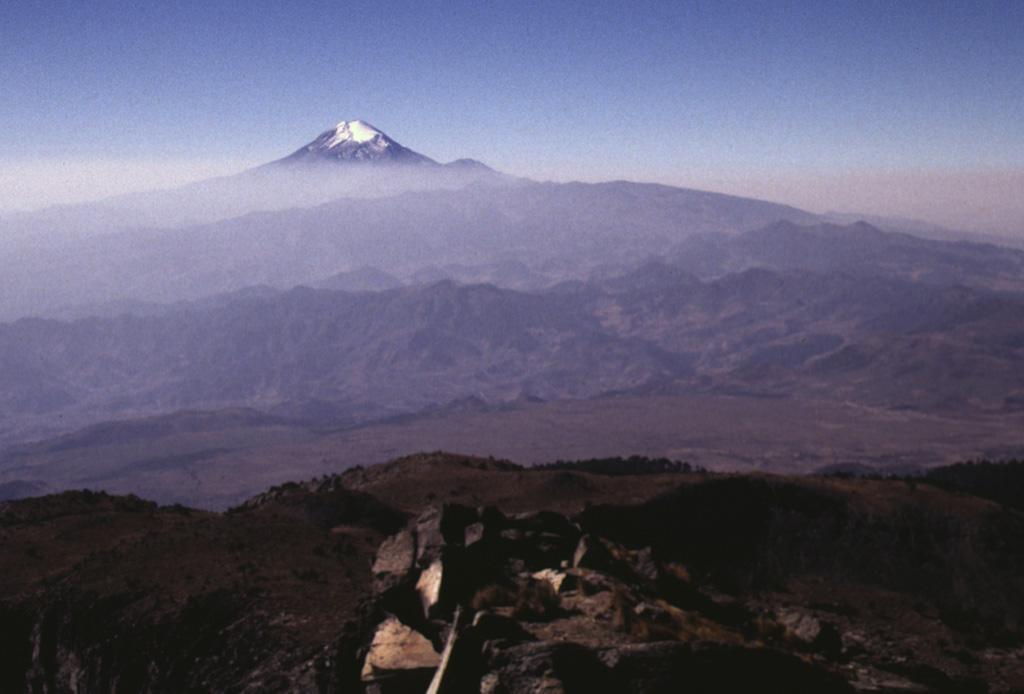 The N-S-trending Cofre de Perote-Pico de Orizaba volcanic chain is perpendicular to the trend of the Mexican Volcanic Belt. This view looking southward from the Cofre de Perote summit towards glacier-capped Pico de Orizaba in the background shows two lesser known volcanic complexes in between. The La Gloria volcanic field, also known as the Desconocido-Tecomales volcanic field, forms the eroded area in the center of the photo, and Las Cumbres volcano is the broad range that extends from in front of Orizaba to the right-center horizon. Photo by Lee Siebert, 1998 (Smithsonian Institution).