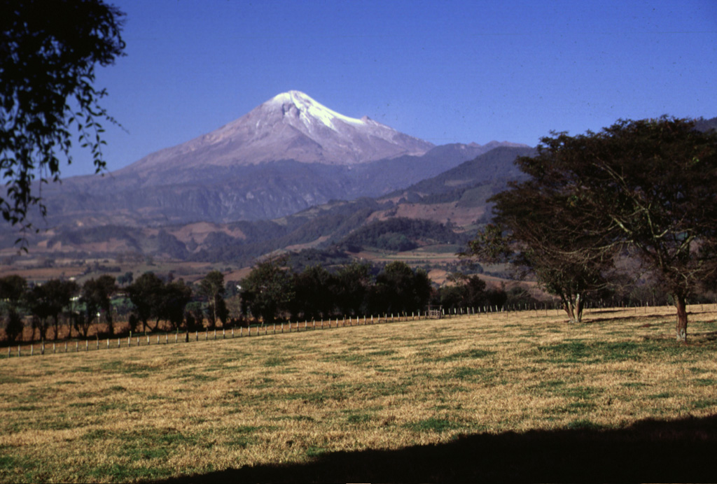 Like other volcanoes in the Cofre de Perote-Pico de Orizaba chain, Orizaba was constructed on the edge of the Altiplano and consequently has higher relief on the eastern side facing the Atlantic coastal plain. Glaciated Orizaba towers 4,200 m above fields near the town of Coscomatepec on its eastern flank. The valley to the left was impacted by the voluminous clay-rich Tetelzingo debris avalanche and lahar during the late Pleistocene. Photo by Lee Siebert, 1998 (Smithsonian Institution).