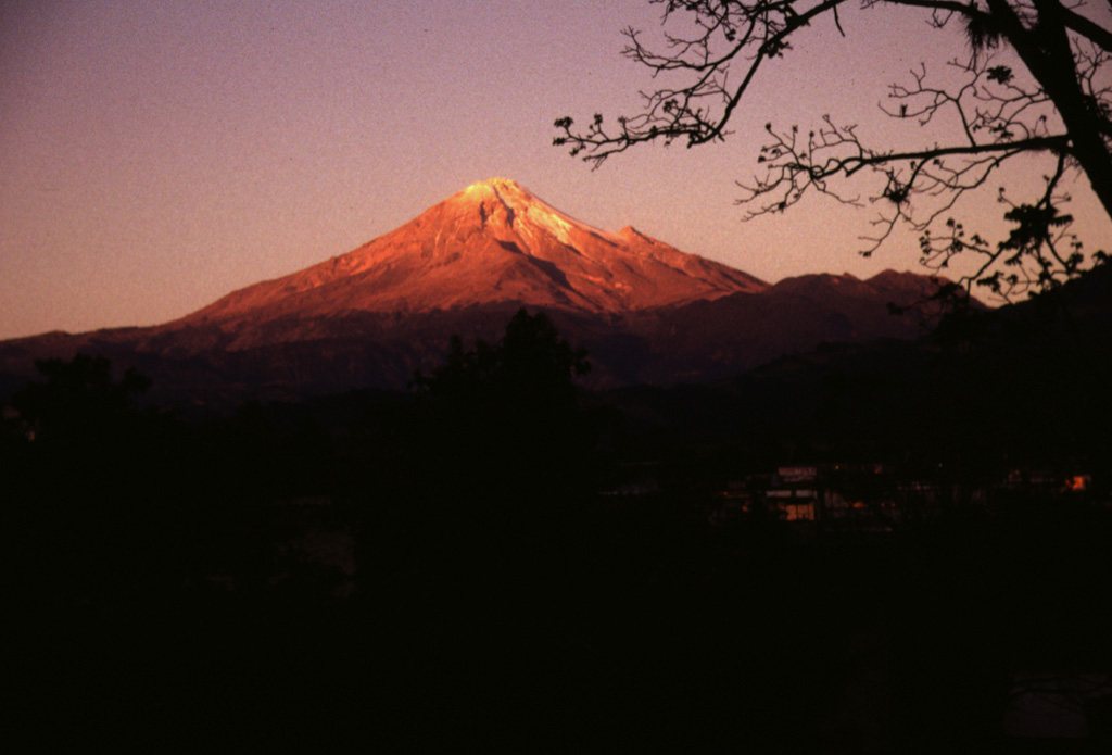 Pico de Orizaba volcano is seen here at sunrise above the town of Calcahualco. The volcano is named for the city of Orizaba below its SE flank, but is also known by the Aztec name of Citlaltépetl (Star Mountain). The volcano has a rich cultural history. Its lower slopes host Aztec villages, pyramids, and temples, and it is depicted in Aztec hieroglyphics. Photo by Lee Siebert, 1998 (Smithsonian Institution).