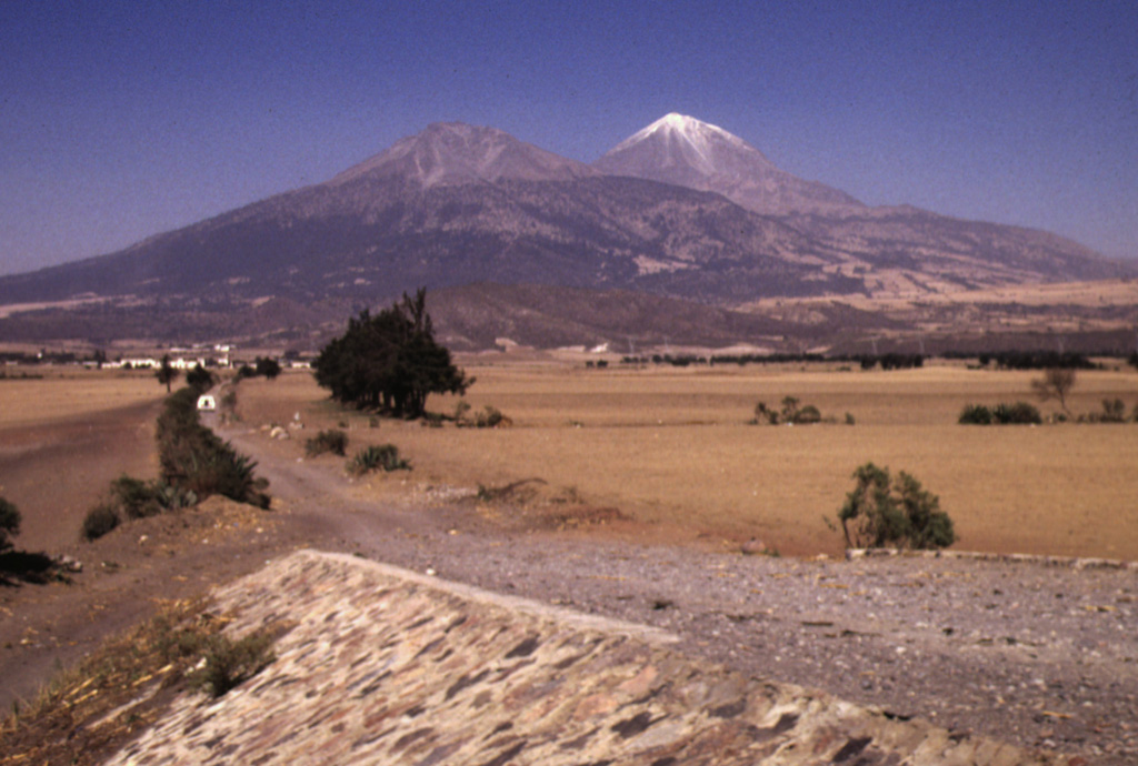 Pico de Orizaba volcano is seen here from the south, with snow-free Sierra Negra volcano to its left. Sierra Negra is the southernmost major vent of the roughly NNE-SSW-trending Pico de Orizaba-Cofre de Perote volcanic chain. The construction of Sierra Negra was contemporaneous with the mid-Pleistocene early stages in the formation of Orizaba volcano. Sierra Negra is composed largely of lava flows and produced numerous pyroclastic flows mainly to the SW and W. Photo by Lee Siebert, 1998 (Smithsonian Institution).