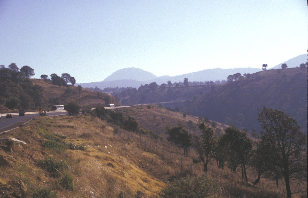 Papayo dome is seen in the center of this photo, a dacite lava dome along the crest of the Sierra Nevada 15 km north of Iztaccíhuatl volcano. The dome, seen here from the west, was the source of a voluminous postglacial lava flow that traveled 9.5 km to the WSW and more than 10 km to ENE. The Mexico City-Puebla highway (left) follows the northern margin of the lava flow, which covers an area of 84 km2. Photo by Lee Siebert, 1997 (Smithsonian Institution).