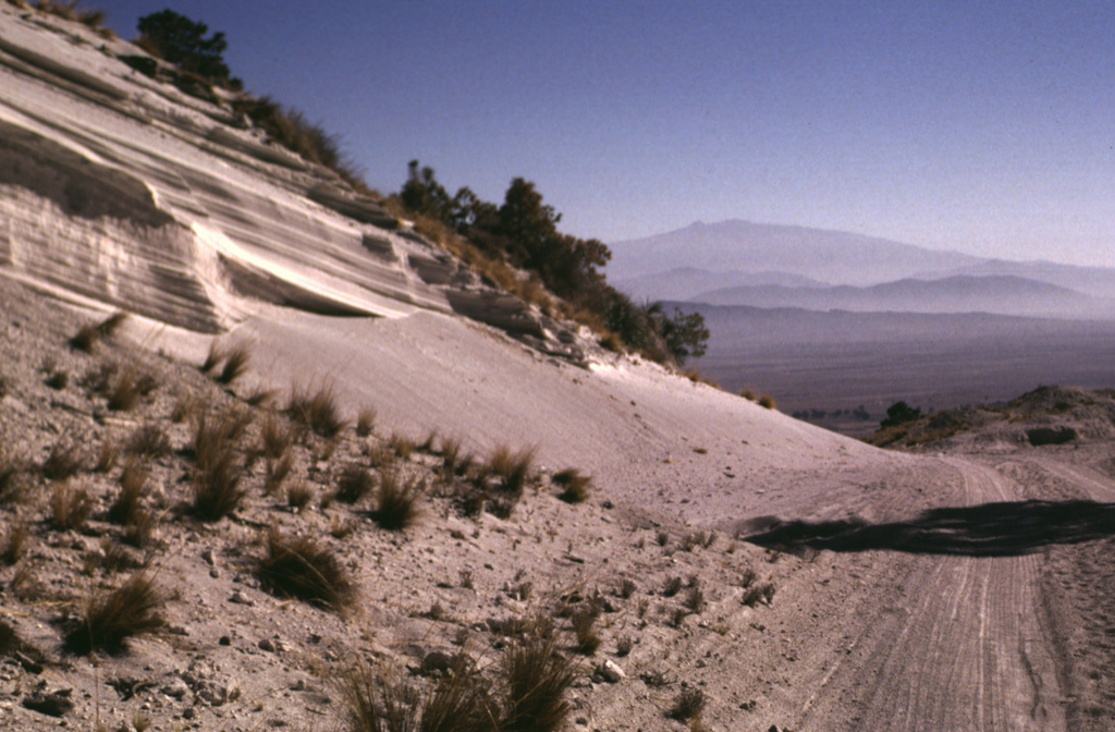 A roadcut through the eastern rim of the Cerro Xalapasco tuff cone exposes pyroclastic-surge deposits. The road provides access to a quarry where perlite (hydrated obsidian) is mined. Cofre de Perote volcano rises on the distant horizon across the Serdán-Oriental basin. Photo by Lee Siebert, 1998 (Smithsonian Institution).
