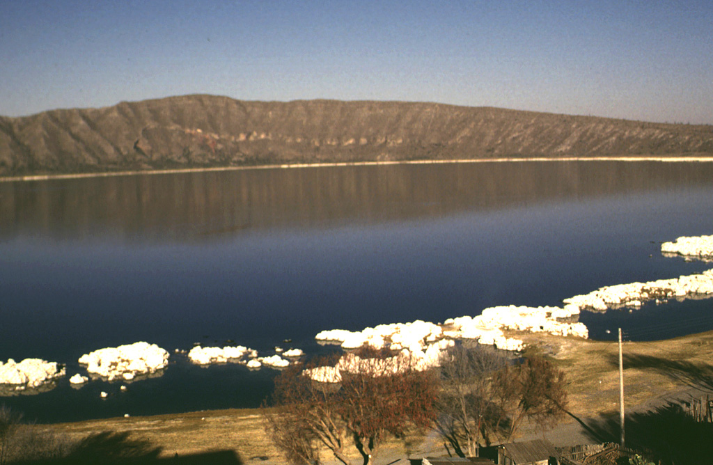 The Laguna Alchichicha maar is filled by the largest lake in the Serdán-Oriental basin. The rim of the basaltic to basaltic-andesitic maar varies in height and is highest on the western side. The western crater wall exposes a scoria cone that was partially destroyed by the maar-forming eruption. White tufa deposits line the shore of the lake. Photo by Lee Siebert, 1997 (Smithsonian Institution).