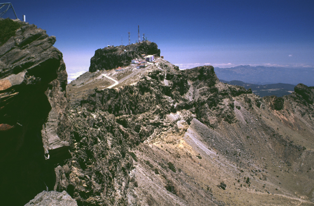 The summit region of Cofre de Perote consists of at least two glacially eroded edifices. Glacial cirques and moraines are found in the summit area. The steep-walled east-facing scarp cutting across the center of the photo that exposes westward-dipping lavas was formed in part by edifice collapse. Photo by Lee Siebert, 1999 (Smithsonian Institution).