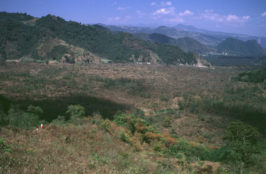 The people in the left foreground are standing on the Toxtlacuaya lava flow, which traveled in a narrow lobe down into the valley filled by the flat-lying Río Naolinco lava flow. Both flows were produced about 900 years ago during a geochemically bimodal eruption which initially produced the alkaline Toxtlacuaya lava flow and then the voluminous calc-alkaline Río Naolinco flow. Although the flows erupted through the lower flanks of Cofre de Perote volcano, they are geochemically distinct from Cofre de Perote lavas. Photo by Lee Siebert, 1999 (Smithsonian Institution).