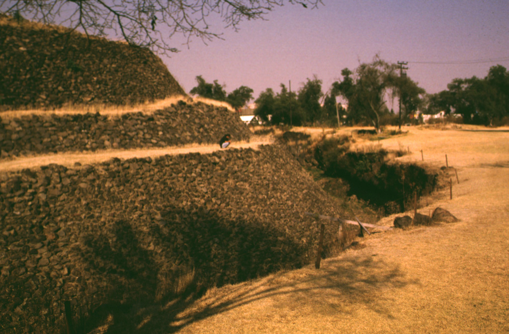 The Cuicuilco pyramid in the southern part of Mexico City was surrounded by lava flows from Xitle volcano about 1,600 years ago. The basaltic flows underlie the area to the right and are exposed in the trench walls around the pyramid. The Preclassic Cuicuilco site is one of the oldest archaeological areas in central México. The earliest occupations date back to 2,100-1,800 BCE, and the pyramid was constructed about 80-600 BCE, when Cuicuilco had become an important Pre-Hispanic city. Photo by Lee Siebert, 1998 (Smithsonian Institution).