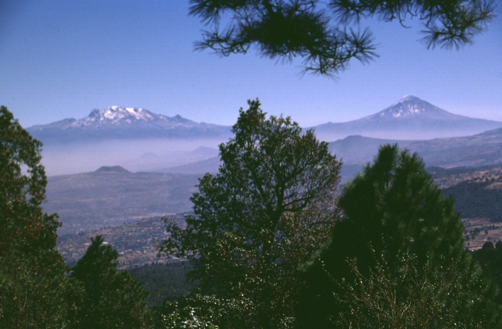 The volcanoes bordering the Valley of Mexico appear in Aztec legend. Popocatépetl (right) is said to hold a funeral torch for Iztaccíhuatl (left), the sleeping "Woman in White." The hills in the foreground (seen from the summit of Xitle scoria cone) are part of the broad Chichinautzin volcanic field south of Mexico City. Chichinautzin means "Burning Lord," a possible reference to eruptive activity. Photo by Lee Siebert, 1997 (Smithsonian Institution).