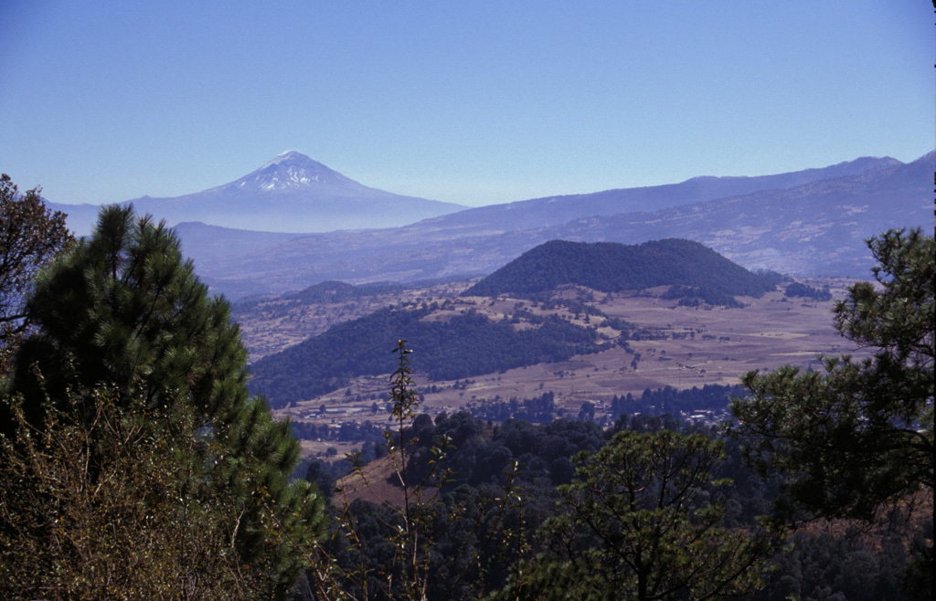 Volcán Popocatépetl rises to the SE beyond the Sierra Chichinautzin, as seen from the summit of Xitle volcano, one of the youngest cones of the Chichinautzin volcanic field. The scoria cone near the center is Volcán Yololica. More than 150 small cones formed across the Chichinautzin range; many of these are of Holocene age.  Photo by Lee Siebert, 1998 (Smithsonian Institution).