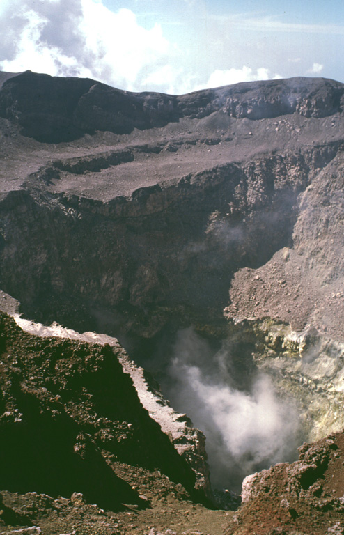 The summit crater of San Miguel volcano reflects a complex sequence of events.  This view from the northern crater rim shows two lava benches that are truncated by a deep compound central pit crater from which steam plumes rise.  The morphology of the summit crater has varied dramatically during historical time.  The inner pit crater has gradually expanded to the east and north and increased in depth to nearly 350 m in 1999. Photo by Lee Siebert, 1999 (Smithsonian Institution).