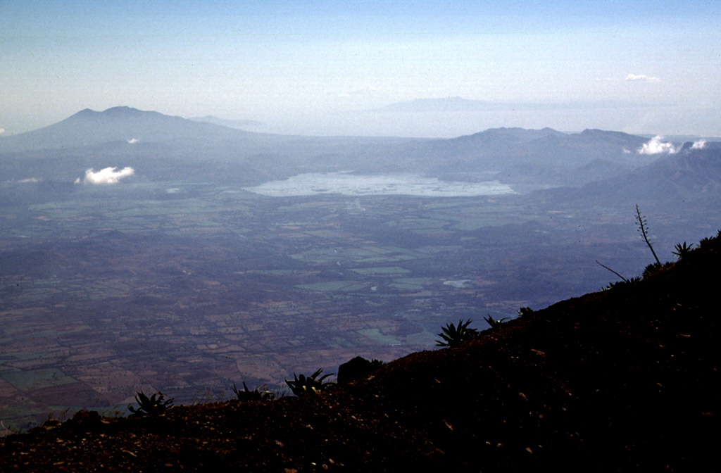 The twin peaks of Volcán Conchagua appear in the distance on the left horizon in this view to the east from the summit of San Miguel volcano.  Conchagua lies on the shore of the Gulf of Fonseca at the SE tip of El Salvador.  The large lake in the center of the photo is Laguna de Olomega.  Flat-topped Cosiqüina volcano in Nicaragua is visible in the far distance at the upper right across the Gulf of Fonseca. Photo by Lee Siebert, 1999 (Smithsonian Institution).