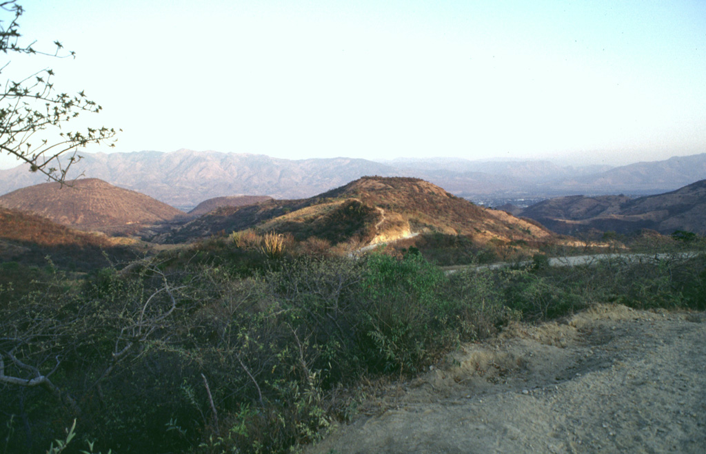 The Chiquimula volcanic field occupies a fault-bounded basin in the Chiquimula Valley of SE Guatemala. Recent eruptions produced basaltic scoria cones and lava flows constructed along a N-S-trending fracture starting near the northern edge of Chiquimula town. Part of the town is seen on the valley floor to the right of the hill in the center of this photo, taken from the NW along the road to Maraxco. Photo by Giuseppina Kysar, 1999 (Smithsonian Institution).