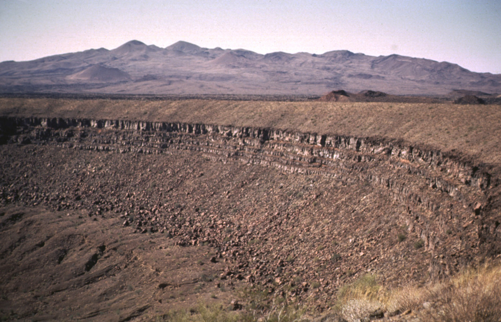 Santa Clara shield volcano, seen on the SW horizon beyond the rim of Cráter Elegante maar, is of late-Pliocene to Pleistocene age. The broad edifice is largely mantled by pyroclastic ejecta and lava flows of the basaltic Pinacate monogenetic volcanic series, which began erupting about 1.2 million years ago. More than 500 scoria cones and associated lava flows have formed across the Pinacate field and extend into the surrounding desert. Photo by Bill Rose, 1969 (Michigan Technological University).