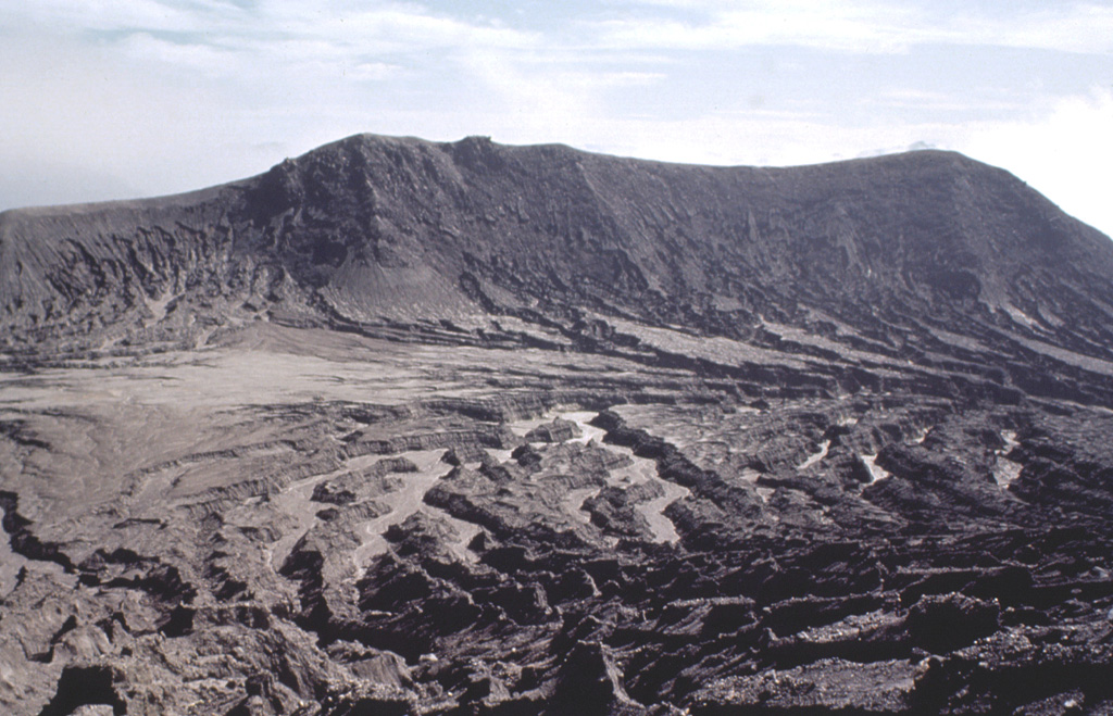 The eastern rim of the 1982 crater at El Chichón is seen here from the rim of the larger, older crater. Erosional gullies formed within pyroclastic flow and surge deposits that traveled radially away from the 1982 crater. The rim rises about 50 m above the moat between the two craters. Prior to the 1982 eruption a lava dome reached several hundred meters above the crater floor. Photo by Bill Rose, 1983 (Michigan Technological University).