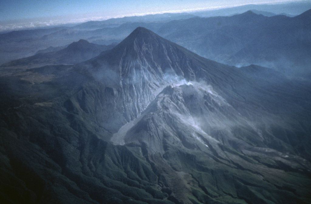 Santa María is one of Guatemala's most active volcanoes. Growth of the degassing Santiaguito lava dome complex began in 1922 at the base of the large crater formed in the Santa María SW flank during a major explosive eruption in 1902. Light-colored volcanic deposits fill the moat to the left of the dome. Lava flows accompanying dome growth descend towards the lower right. The lower peak behind and to the left of Santa María is Cerro Quemado, a lava dome complex within the Almolonga caldera. Photo by Bill Rose, 1980 (Michigan Technological University).