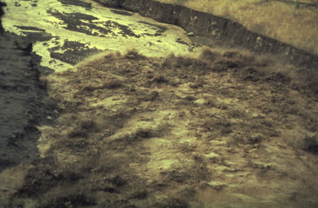 The advancing front of a lahar travels down the Río Nimá Segundo below the Santiaguito lava dome complex on 14 August 1989. Sediment yields in drainages below the Santa Maria’s active domes are extremely high, and rainy season lahars frequently impact areas downstream. Photo by Jeff Marso, 1989 (Michigan Technological University).